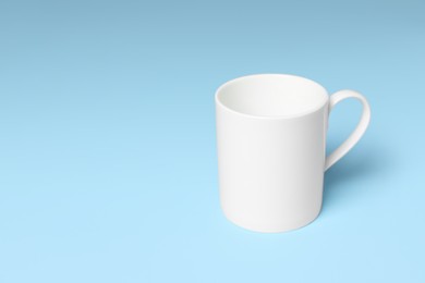 Photo of White ceramic mug on light blue background, space for text