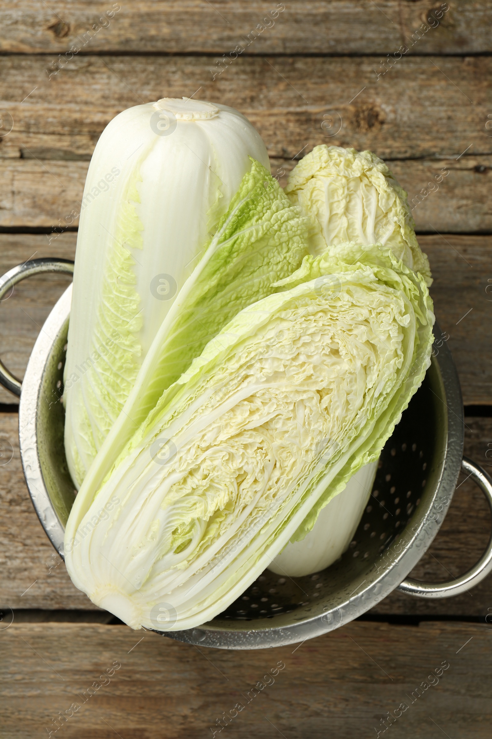 Photo of Whole and cut fresh Chinese cabbages in colander on wooden table, top view