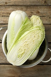 Photo of Whole and cut fresh Chinese cabbages in colander on wooden table, top view