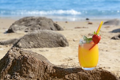 Photo of Glass of refreshing drink with strawberry on beach near sea, space for text