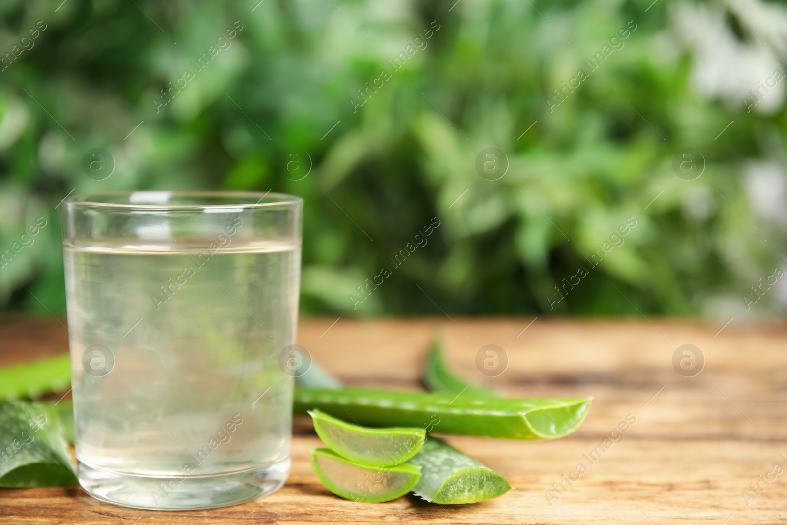 Photo of Fresh aloe drink in glass and leaves on wooden table, space for text