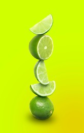 Image of Stacked whole and cut limes on yellowish green background