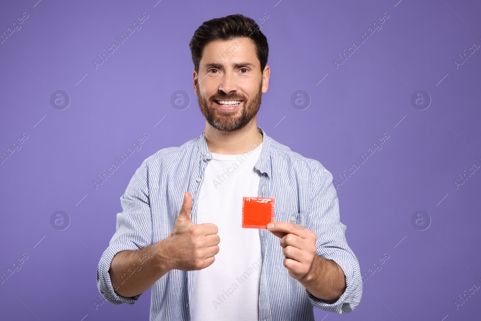 Photo of Happy man with condom showing thumb up on purple background. Safe sex