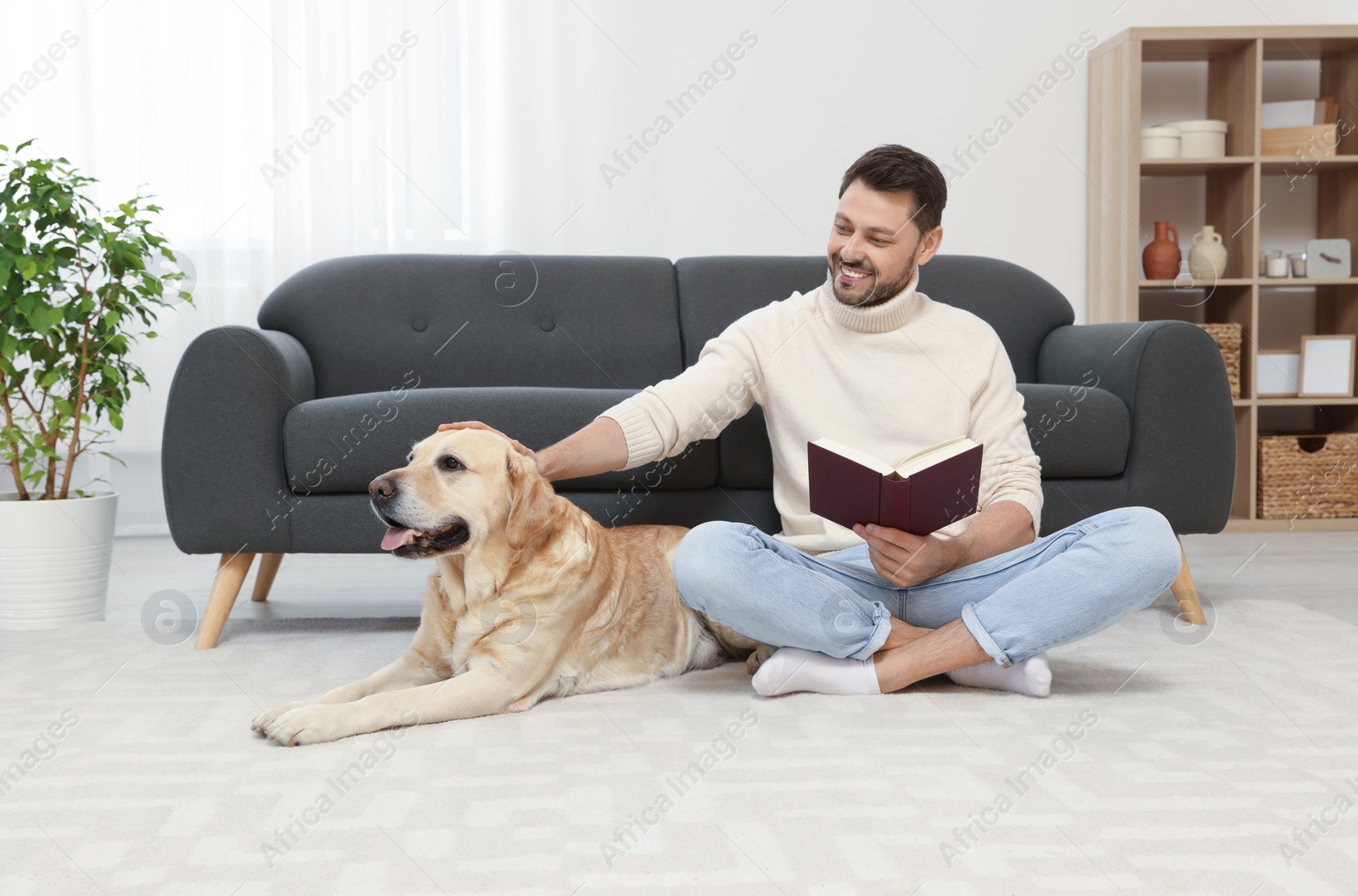 Photo of Man reading book on floor near his cute Labrador Retriever at home