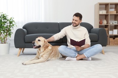 Photo of Man reading book on floor near his cute Labrador Retriever at home