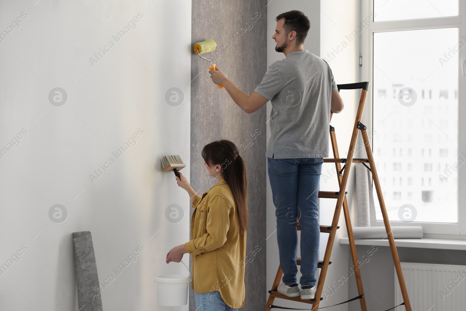 Photo of Woman and man hanging wallpaper in room