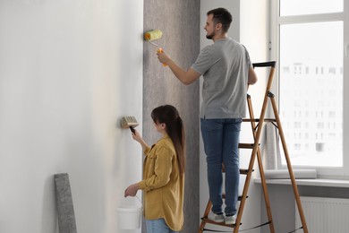 Woman and man hanging wallpaper in room