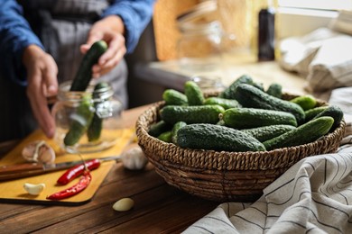 Photo of Woman pickling vegetables at table, focus on basket with cucumbers