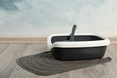 Photo of Cat litter tray with scoop on floor near light blue wall. Space for text
