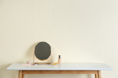 Photo of Mirror and makeup products on white table near light wall. Space for text