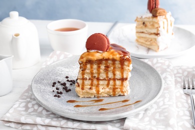 Photo of Piece of delicious homemade cake with caramel sauce and macaron on table