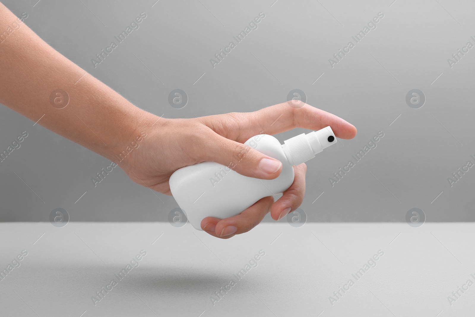 Photo of Woman with bottle of insect repellent spray on grey background, closeup