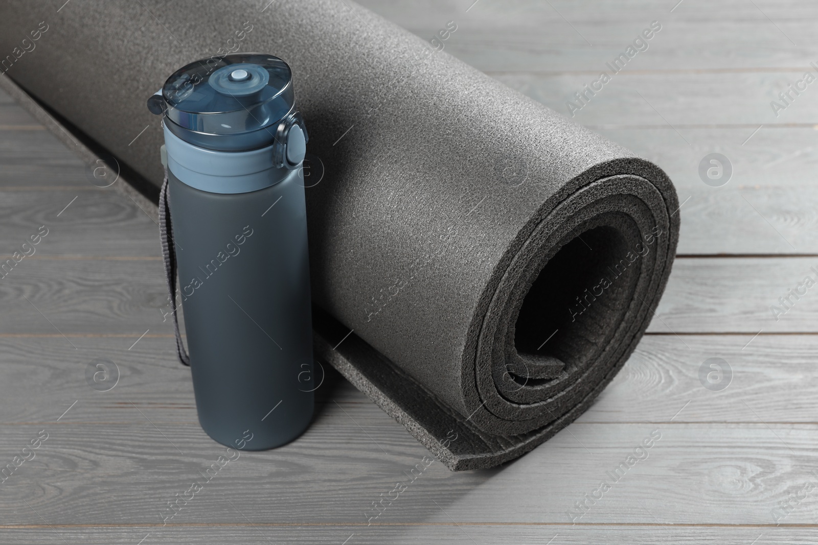 Photo of Yoga mat and bottle of water on grey wooden floor