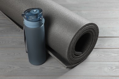 Yoga mat and bottle of water on grey wooden floor