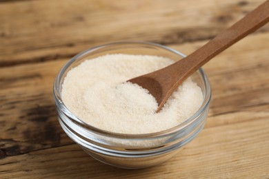 Photo of Glass bowl with gelatin powder and spoon on wooden table, closeup