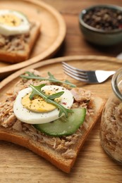 Delicious sandwich with tuna, greens, cucumber, boiled egg and spices on wooden board, closeup