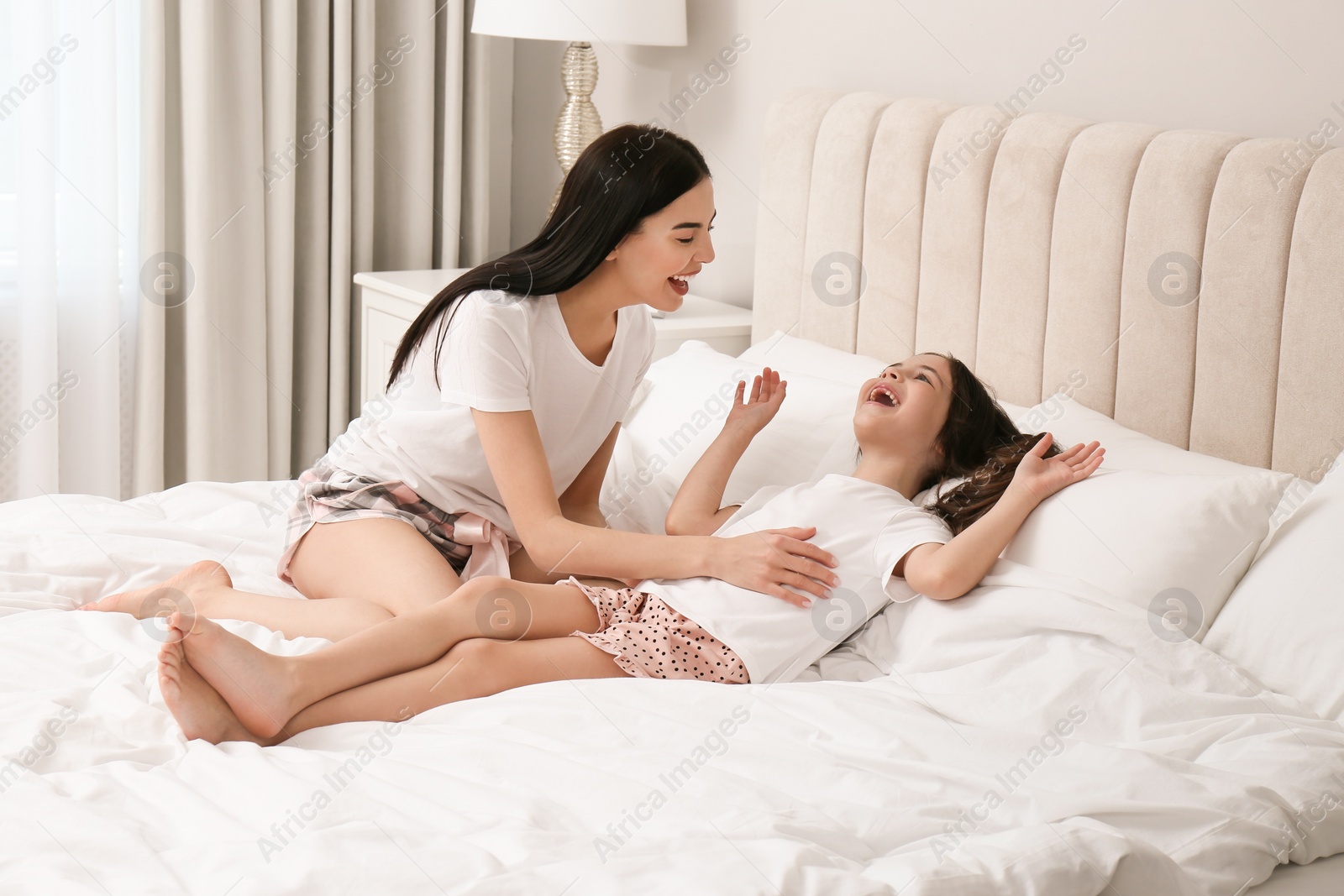 Photo of Young mother and her daughter having fun on bed at home