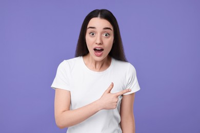 Photo of Portrait of surprised woman pointing at something on violet background