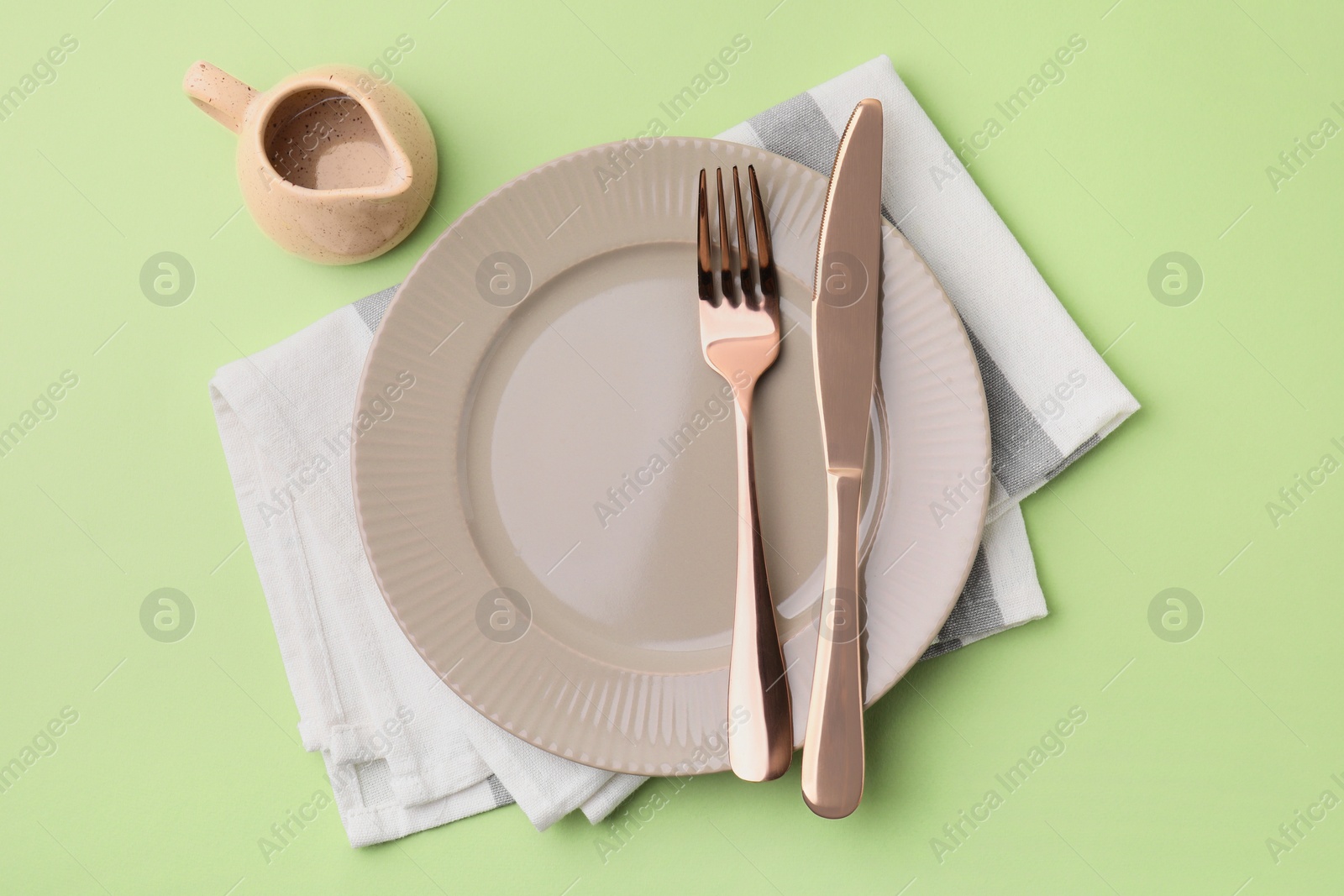 Photo of Clean plate with cutlery, saucepan and napkin on light green background, flat lay