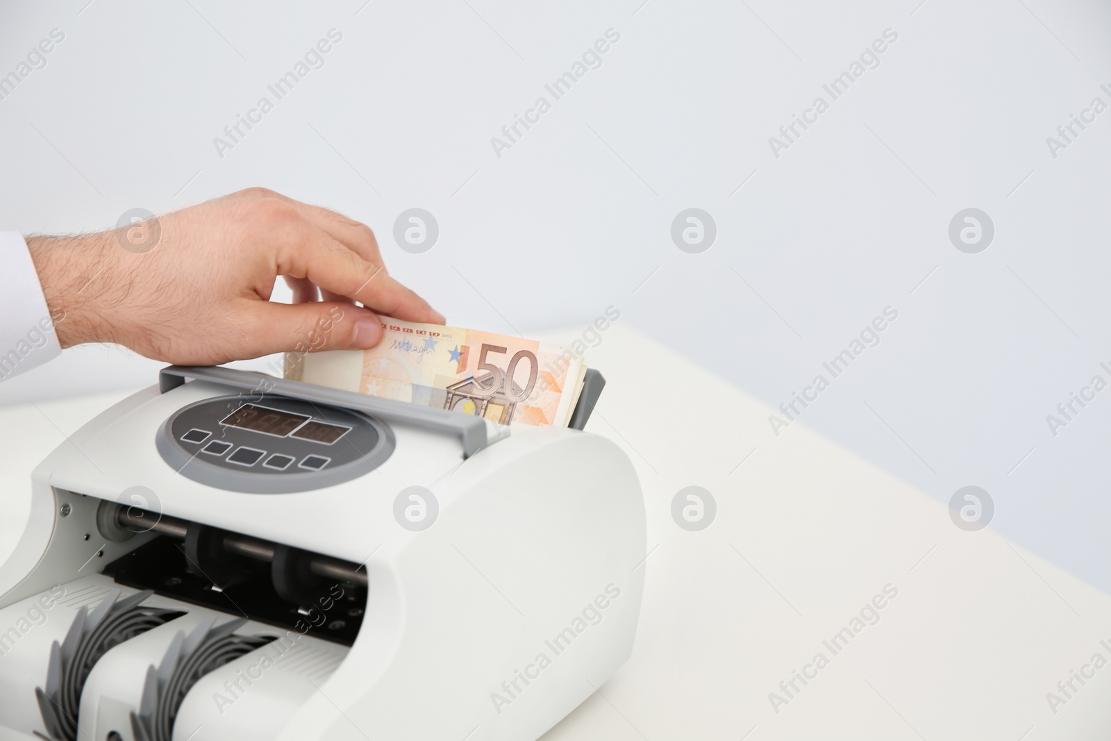 Photo of Man putting money into counting machine on table, closeup. Space for text