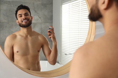 Man spraying luxury perfume near mirror indoors