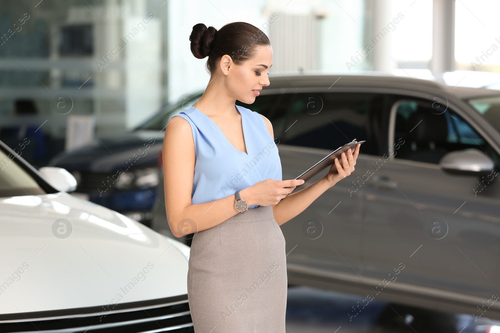 Photo of Young saleswoman with clipboard in car dealership