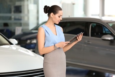 Young saleswoman with clipboard in car dealership