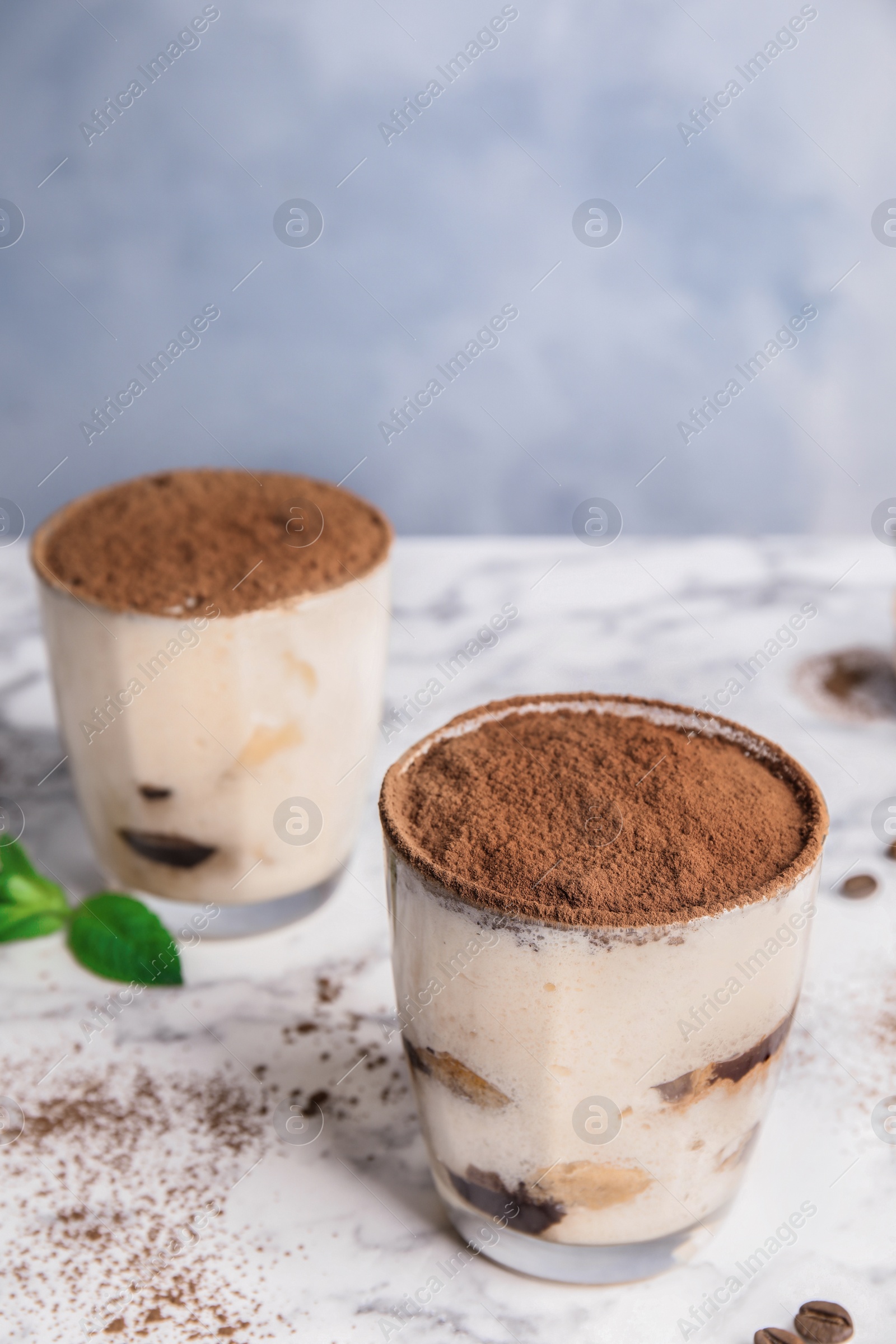 Photo of Two glasses of tiramisu cake on table against color background