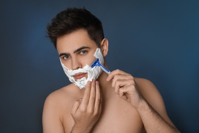 Photo of Handsome young man shaving with razor on blue background