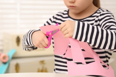 Girl cutting pink paper at desk in room, closeup. Home workplace