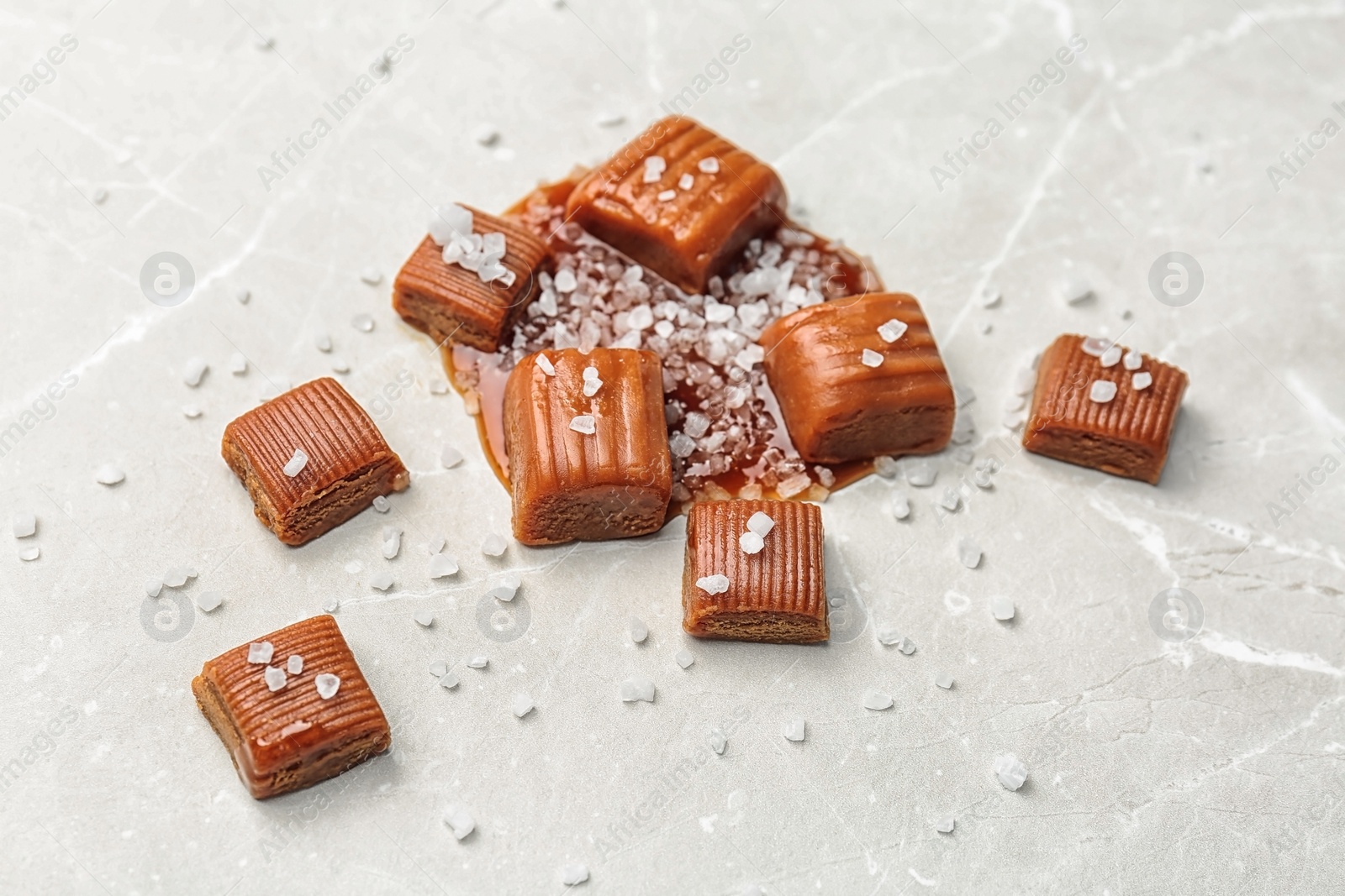 Photo of Delicious candies with salted caramel sauce on light background