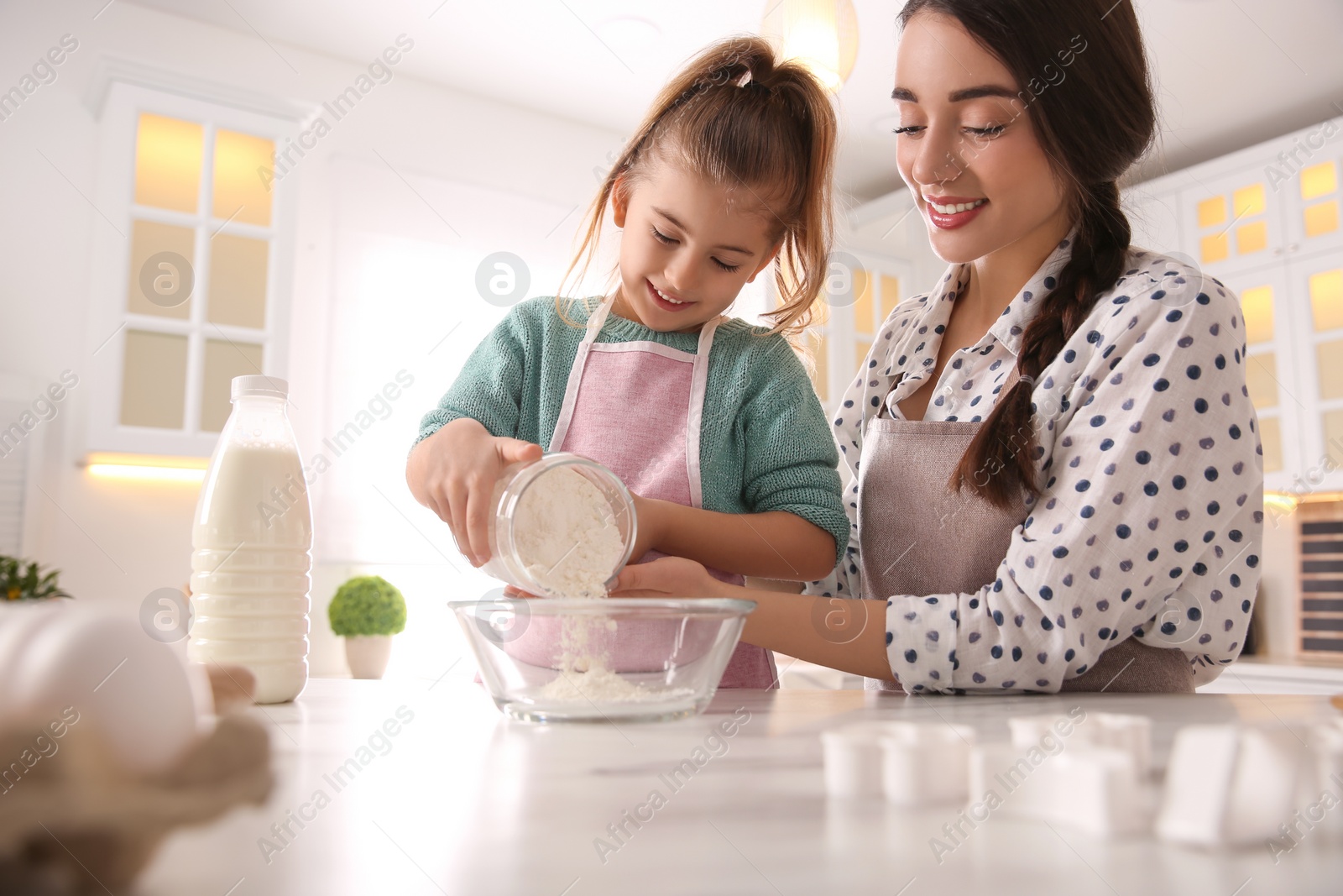 Photo of Mother and daughter making dough at table in kitchen