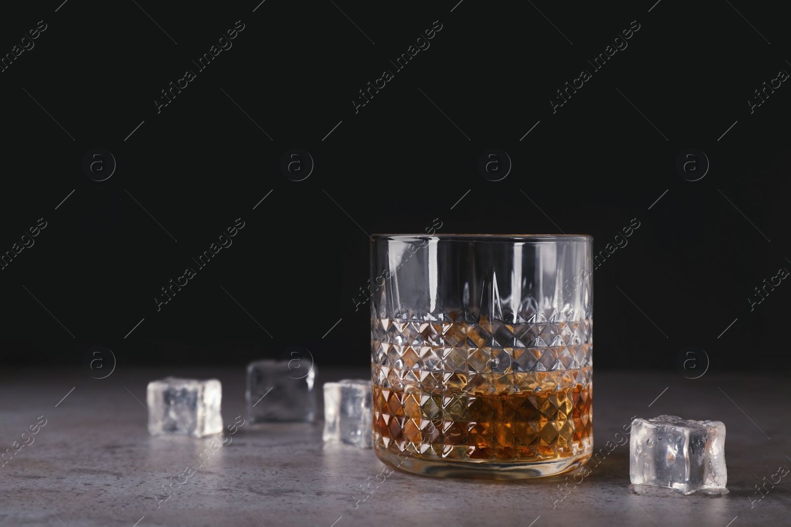 Photo of Golden whiskey in glass with ice cubes on table. Space for text