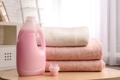 Photo of Bottle of detergent and clean towels on table indoors. Laundry day
