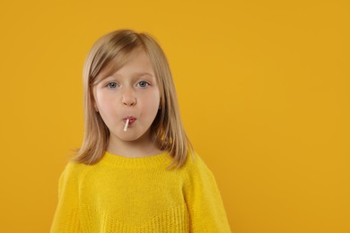 Photo of Cute girl with lollipop on orange background, space for text