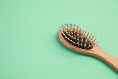 Photo of Wooden brush with lost hair on green background, closeup. Space for text