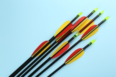 Photo of Many arrows on light blue background, flat lay. Archery sport equipment