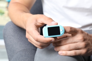 Photo of Young man checking pulse with blood pressure monitor on finger, closeup
