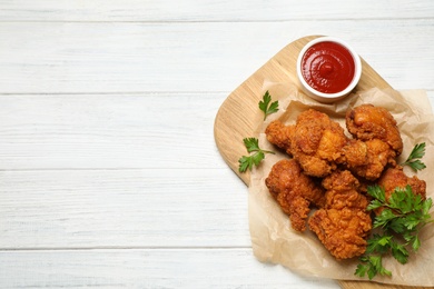 Photo of Tasty deep fried chicken pieces served on white wooden table, top view. Space for text