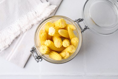 Photo of Tasty fresh yellow baby corns in glass jar on white tiled table, top view