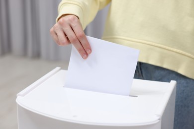 Woman putting her vote into ballot box on blurred background, closeup