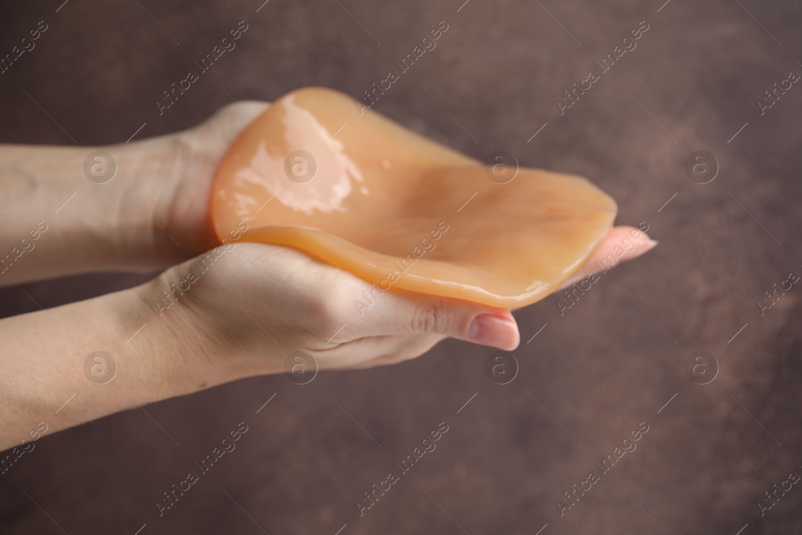 Photo of Making kombucha. Woman holding Scoby fungus on brown background, closeup