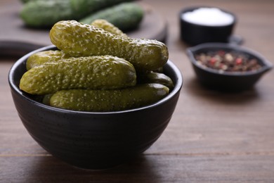 Photo of Bowl of pickled cucumbers and ingredients on wooden table, closeup