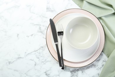 Photo of Clean plates, bowl and cutlery on white marble table, top view. Space for text