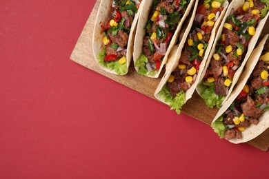 Photo of Delicious tacos with meat and vegetables on red table, top view. Space for text
