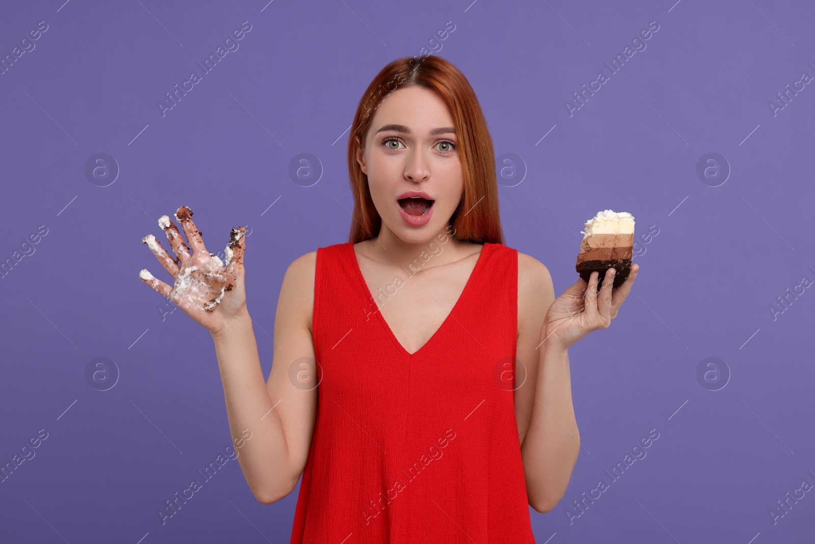 Photo of Emotional young woman with piece of tasty cake and dirty hand on purple background