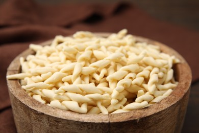 Photo of Uncooked trofie pasta in bowl against blurred background, closeup