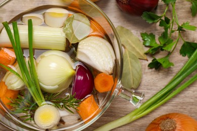 Photo of Glass pot with tasty bouillon and different ingredients on wooden table, flat lay