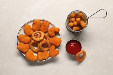 Photo of Tasty fried onion rings, chicken nuggets, cheese sticks and ketchup on light grey marble table, flat lay