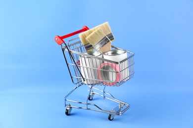 Photo of Small shopping cart with set of painting tools on light blue background